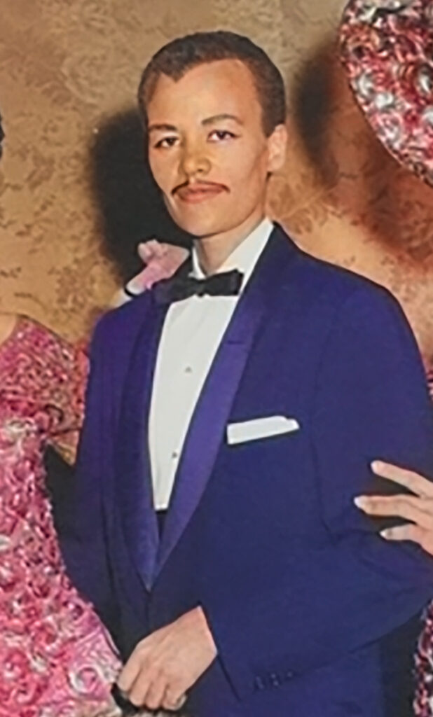 Cropped, colorized photograph of Stormé in her male persona--she has her hair dark and cropped short, like a man's haircut, has a pencil mustache and is wearing a royal blue tuxedo style jacket with a white shirt and a black bow tie