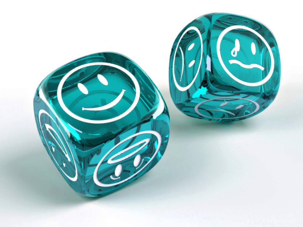 Images is of a pair of transluscent teal dice with a different emotion emoji on each face --exposed are a smiley face on one dice, the other dice is perched on a corner showing a sad face with a tear from  one eye and a frowning face