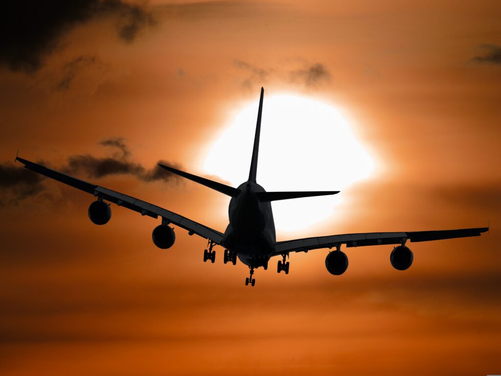 Photograph of a passenger jet taking off against a sunset and orange sky