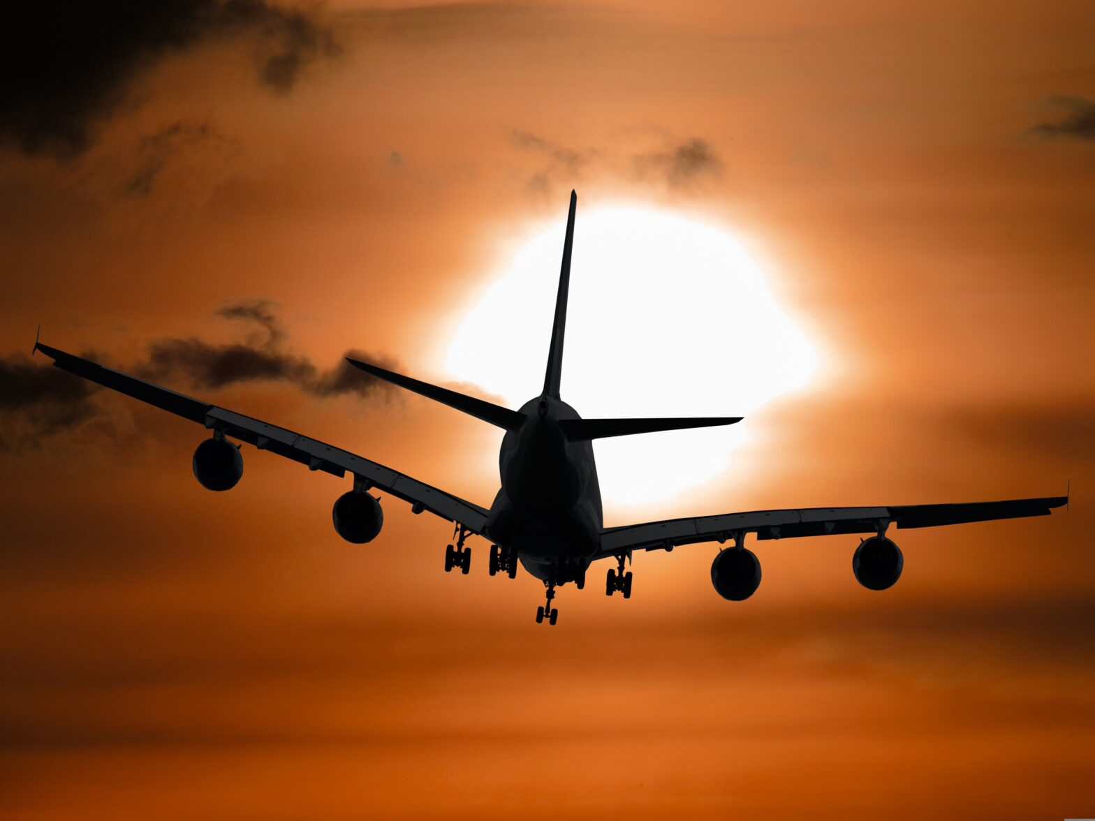 Photograph of a passenger jet taking off against a sunset and orange sky