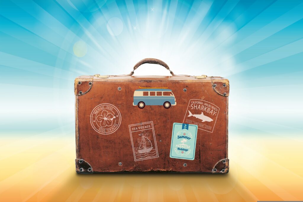 Photographic illustration of a brown leather suitcase with travel stickers on the side sitting on a yellow beach blocking the sun with white rays radiating out against a blue sky on the horizon