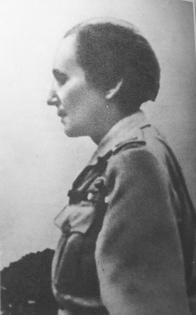 Wanda standing in profile, wearing a uniform and looking to the reader's left